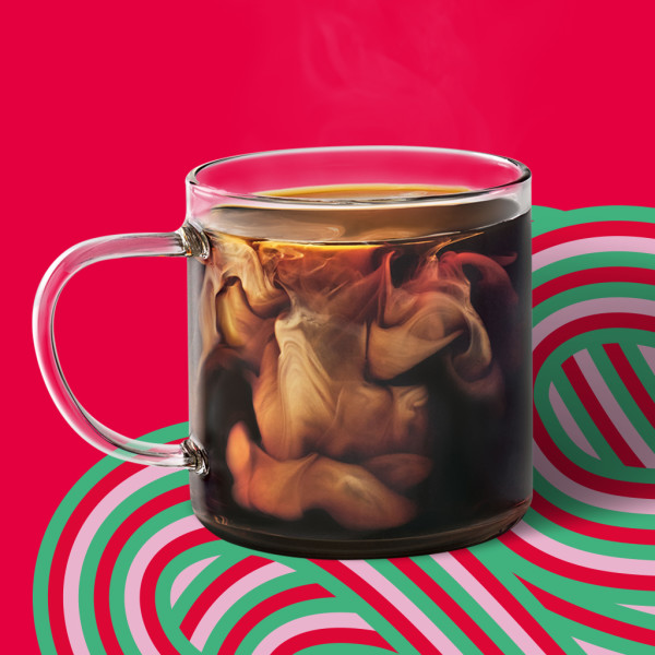 A glass mug of coffee with cream swirling in it on a candy cane type swirl in a colorful setting.