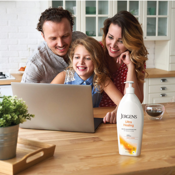 Family sitting around a laptop computer with a bottle of lotion next to it