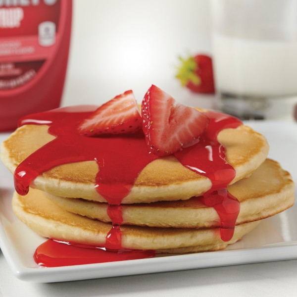 A stack of pancakes with Hershey's strawberry flavored syrup and fresh strawberries