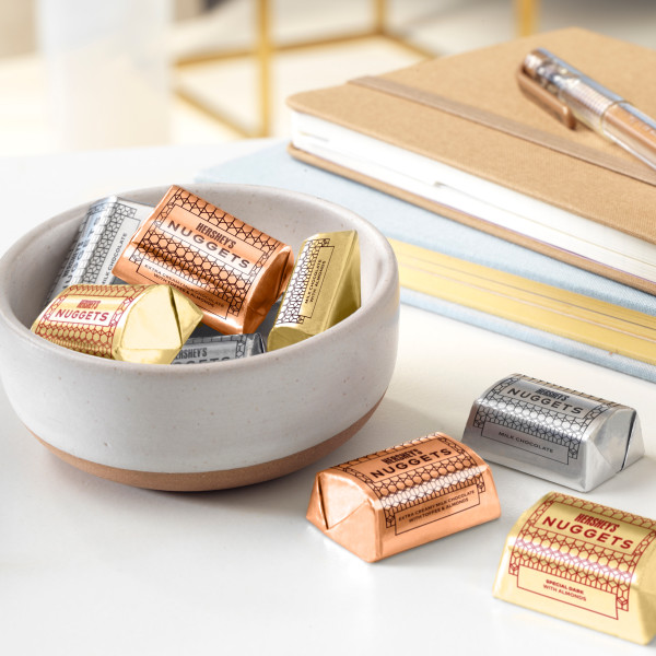 A bowl of HERSHEY'S NUGGETS candies on a desk with a few candies scattered around