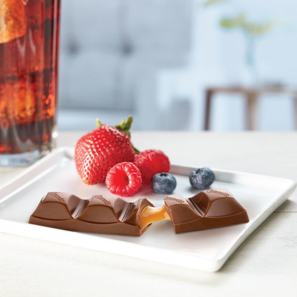 Pieces of a Cadbury Caramello chocolate bar with mixed berries and an iced drink