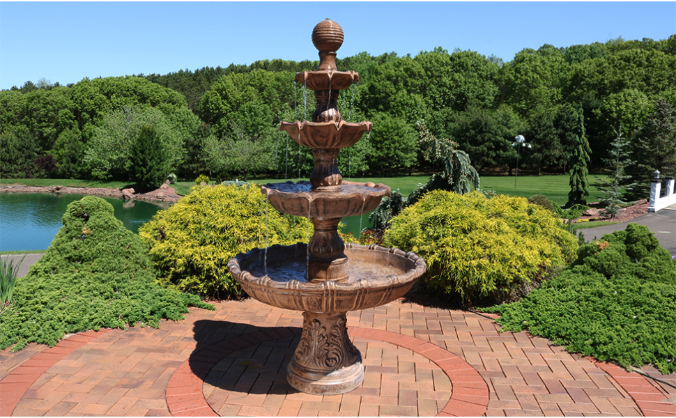 a landscaped backyard centered on a large waterfall fountain framed by colorful shrubs and lawn