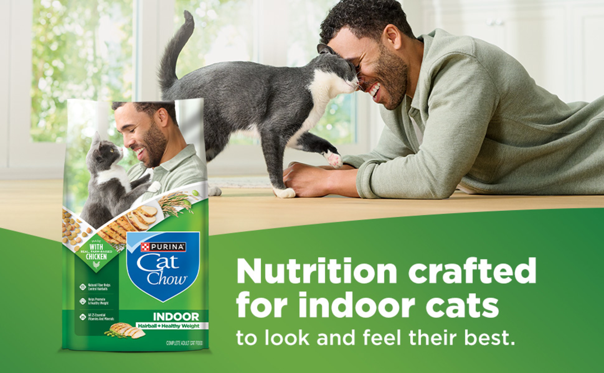 A man lying on the floor interacts with a gray and white cat in a bright home setting. A bag of Purina Cat Chow Indoor is shown in the foreground.