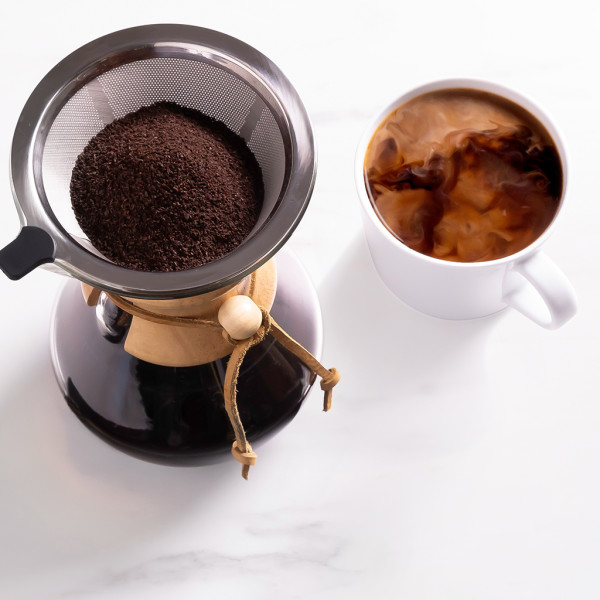 A funnel of coffee grounds on top of a coffee maker next to a mug of black coffee with a cream swirl