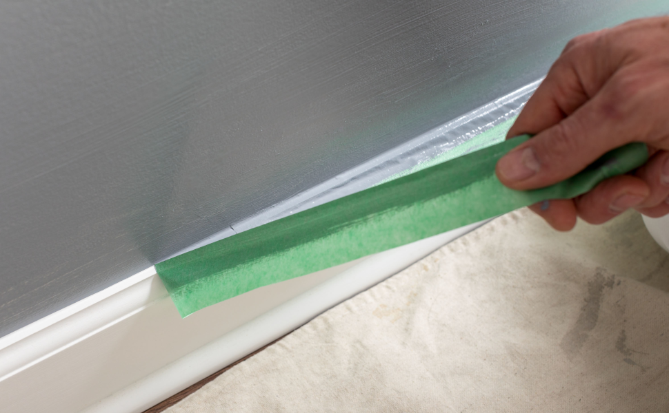 Hand pullling green painter's mate masking tape to reveal a clean paint line