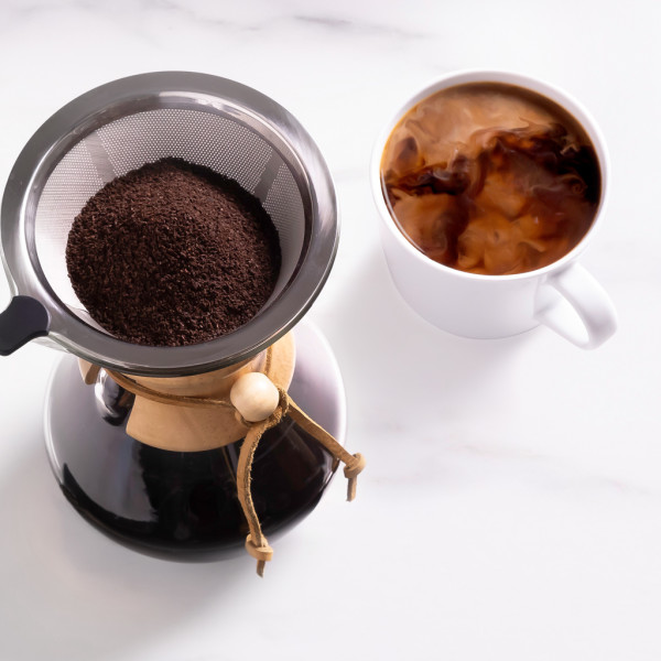 A funnel of coffee grounds on top of a coffee maker next to a mug of black coffee with a cream swirl	