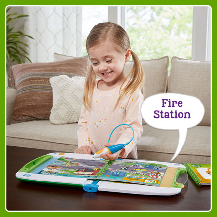 Girl uses stylus to point at words and illustrations in book. LeapStart says: Fire Station.
