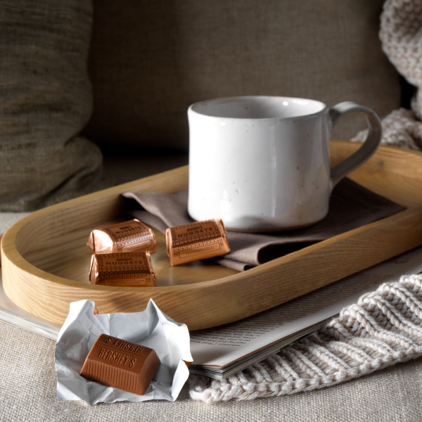 A tray with a mug and an assortment of HERSHEY'S NUGGETS candies on top of a cozy blanket