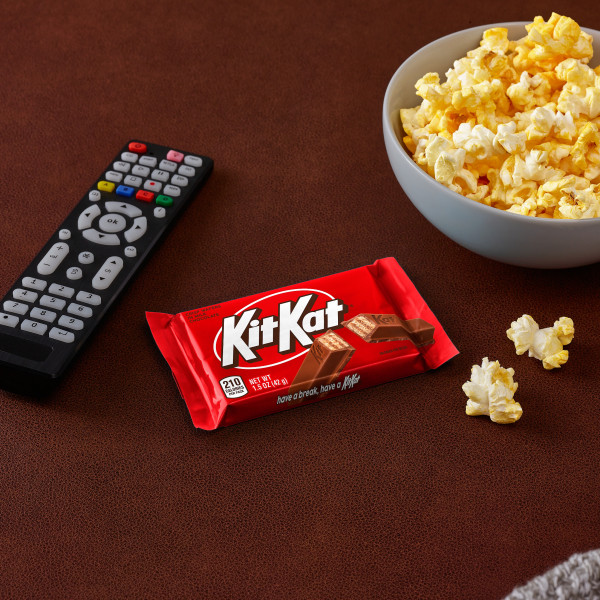 A Kit Kat® candy bar placed between a television remote and bowl of popcorn