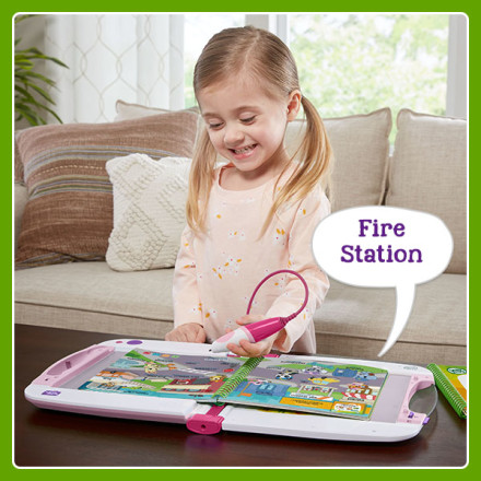 Girl uses stylus to point at words and illustrations in book. LeapStart says: Fire Station.