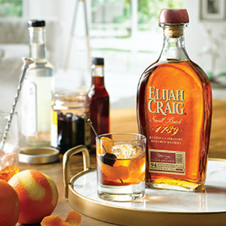 Eljah Craig Small Batch bottle with old fashioned on a tray. Ingredients for cockatil in background.