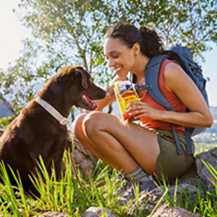 Image of a woman feeding her dog a treat while outside on a hike.