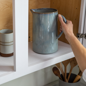 a hand putting a blue pitcher on a shelf with white shelf liner