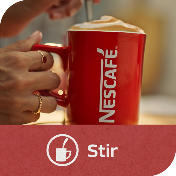 A woman holding a red NESCAFÉ mug and stirring the coffee with a spoon. Tagline: Stir.
