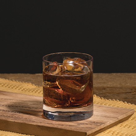 Evan and Cola cocktail in a rocks glass sitting on a dark wooden counter