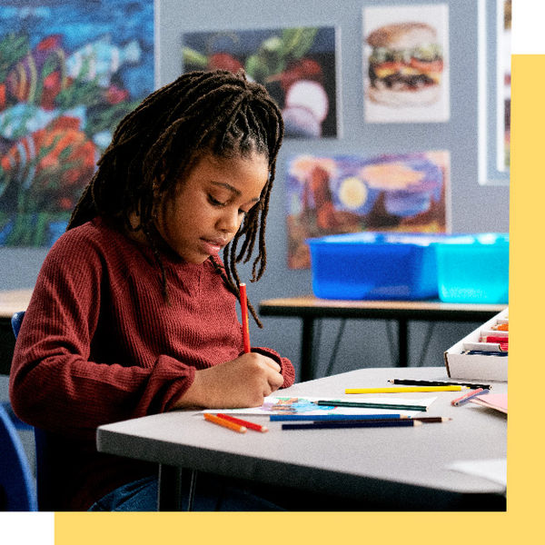 Student sketching with colored pencils during a classroom art activity.