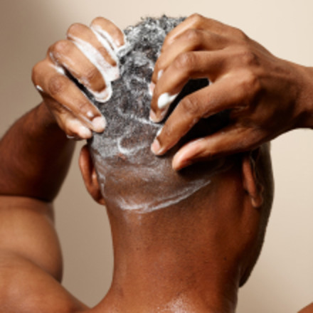 Man washing hair with Suave Citrus Rush 3-in-1, hands lathering foam in curls, fresh & clean.